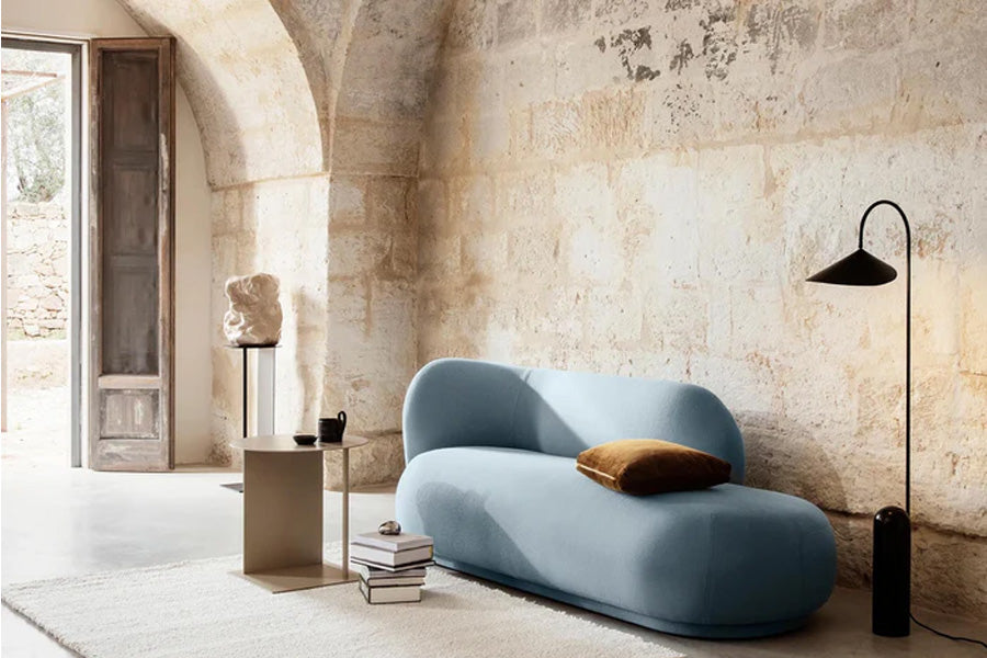 Rico Divan von ferm LIVING in Off-White Bouclé, mit geschwungener Rückenlehne und asymmetrischem Design, in einem modernen Wohnzimmer platziert.