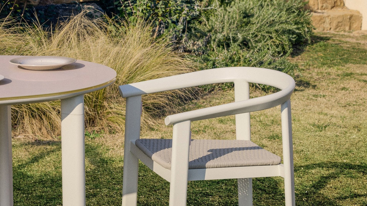 Gartentischset Erice von Kave Home mit stapelbaren Stühlen aus Aluminium und Seil und ovalem Glastisch auf der Terrasse