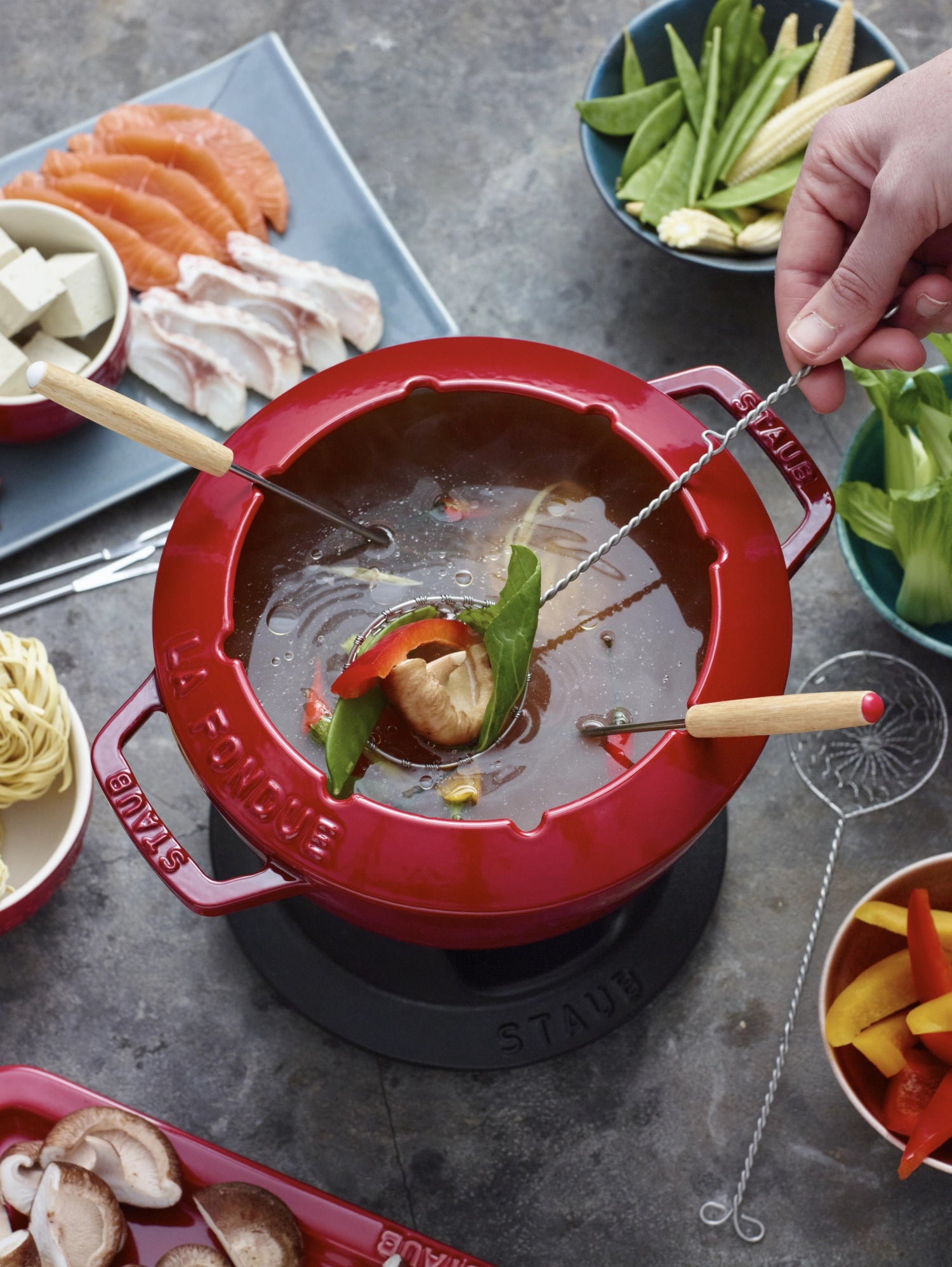 Rotes Fondue Set von Staub mit zwei Griffen, rund und 18 cm Durchmesser, ideal für gesellige Abende und köstliche Fondue-Momente.