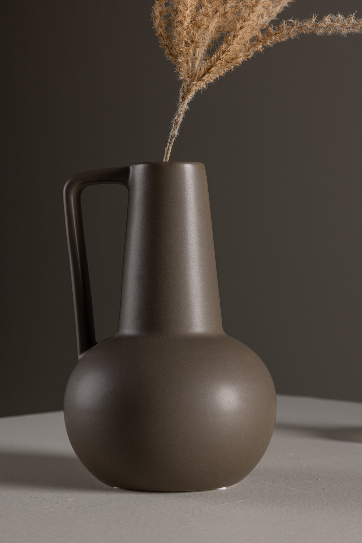 Zylindrische Vase aus Steinzeug in Beige und Schwarz mit seitlichem Griff, matte Oberfläche, Höhe 22 cm, Durchmesser 10 cm.