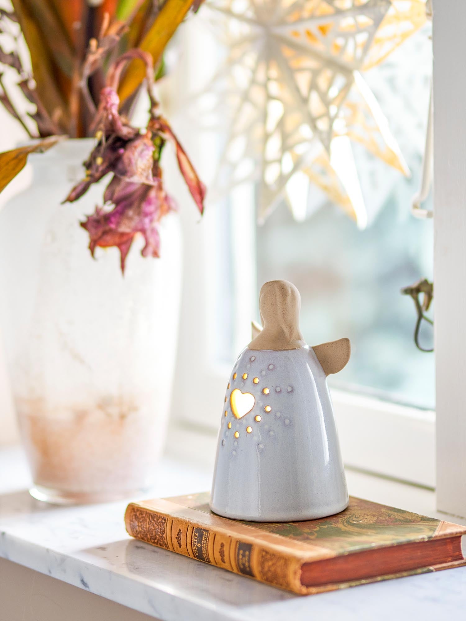 Elegante Engelsfigur aus weissem Steingut mit sanfter Beleuchtung, ideal als stilvolles Dekoelement.