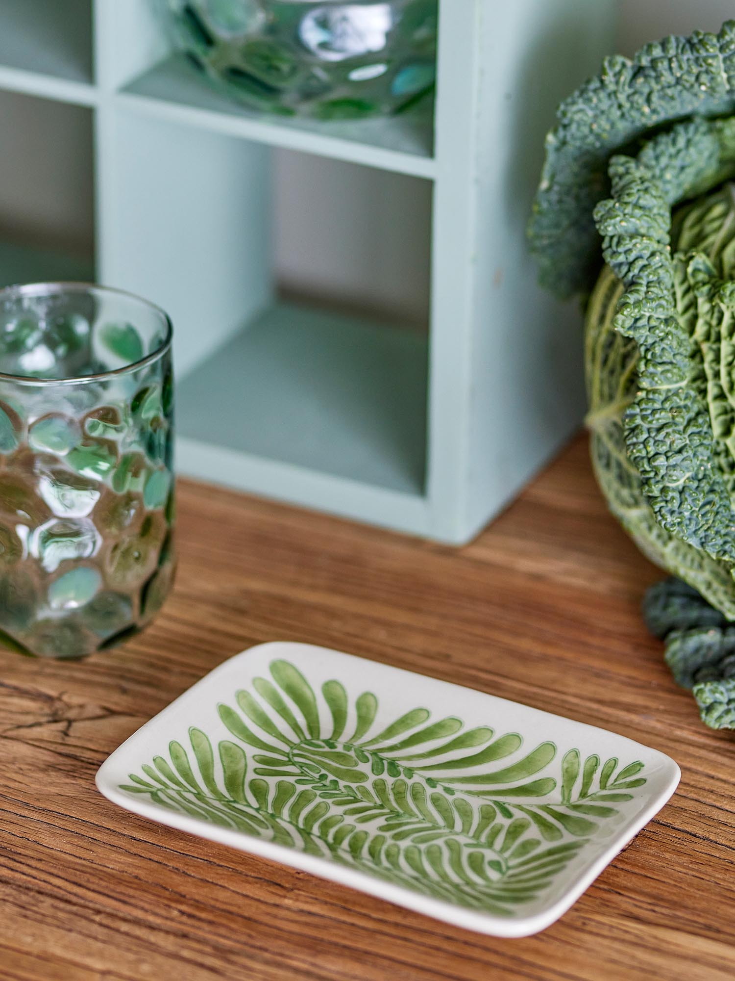 Der Fauni Teller besticht durch sein modernes, rechteckiges Design und das handbemalte grüne Pflanzenmotiv.
