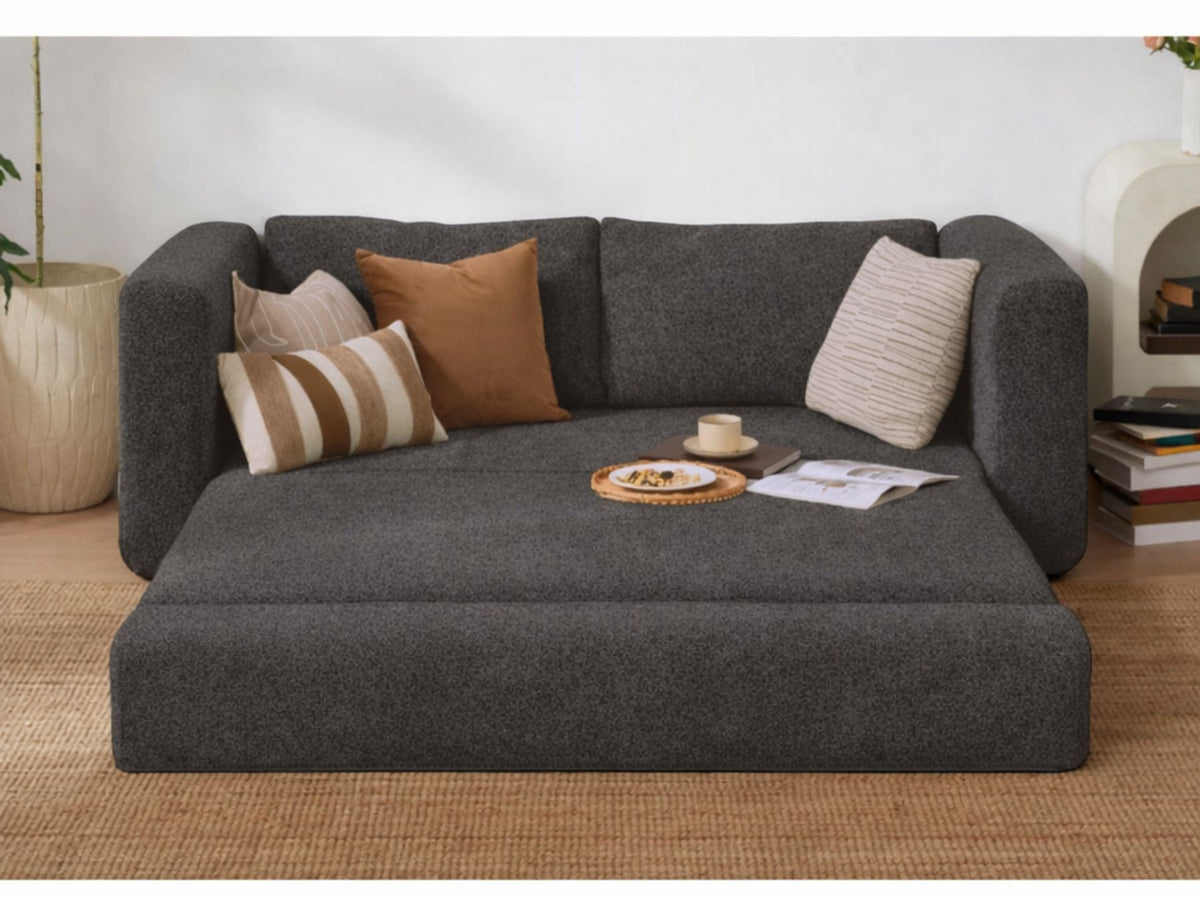 Anthrazitfarbenes 2-Sitzer Schlafsofa Wello aus Bouclé-Stoff mit kompakter Form, Armlehnen und flacher Sitzfläche, aufgestellt im Wohnraum.