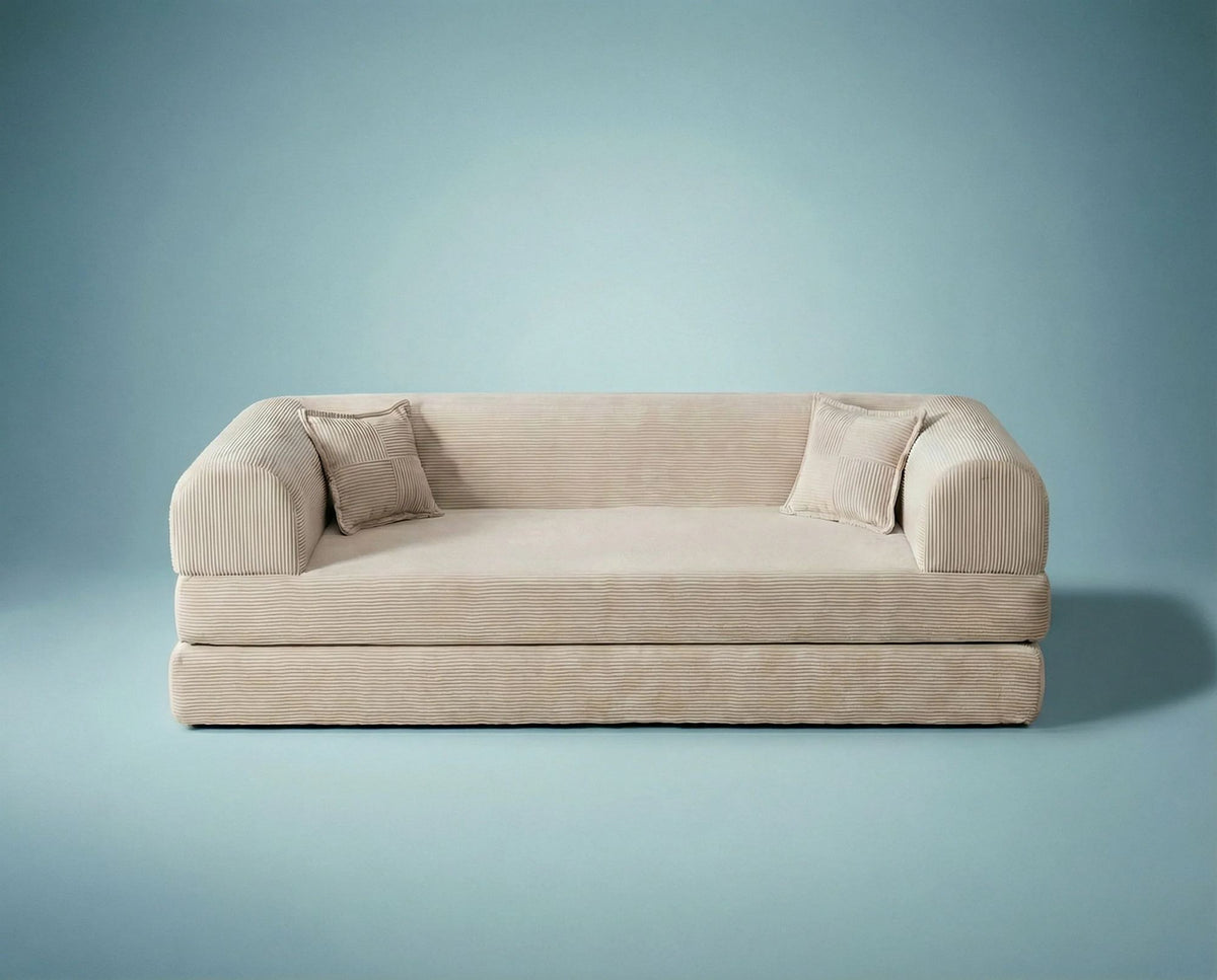 Cremefarbenes 3-Sitzer Schlafsofa Legom Eco von Hanah Home aus geripptem Cord-Plüschstoff mit zwei Kissen im Roll-Pack-Design abgebildet.