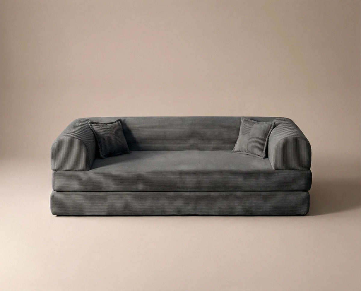 Anthrazitfarbenes 3-Sitzer Schlafsofa aus geripptem Cord-Plüschstoff mit zwei Kissen und sichtbarer rutschfester Sohle.