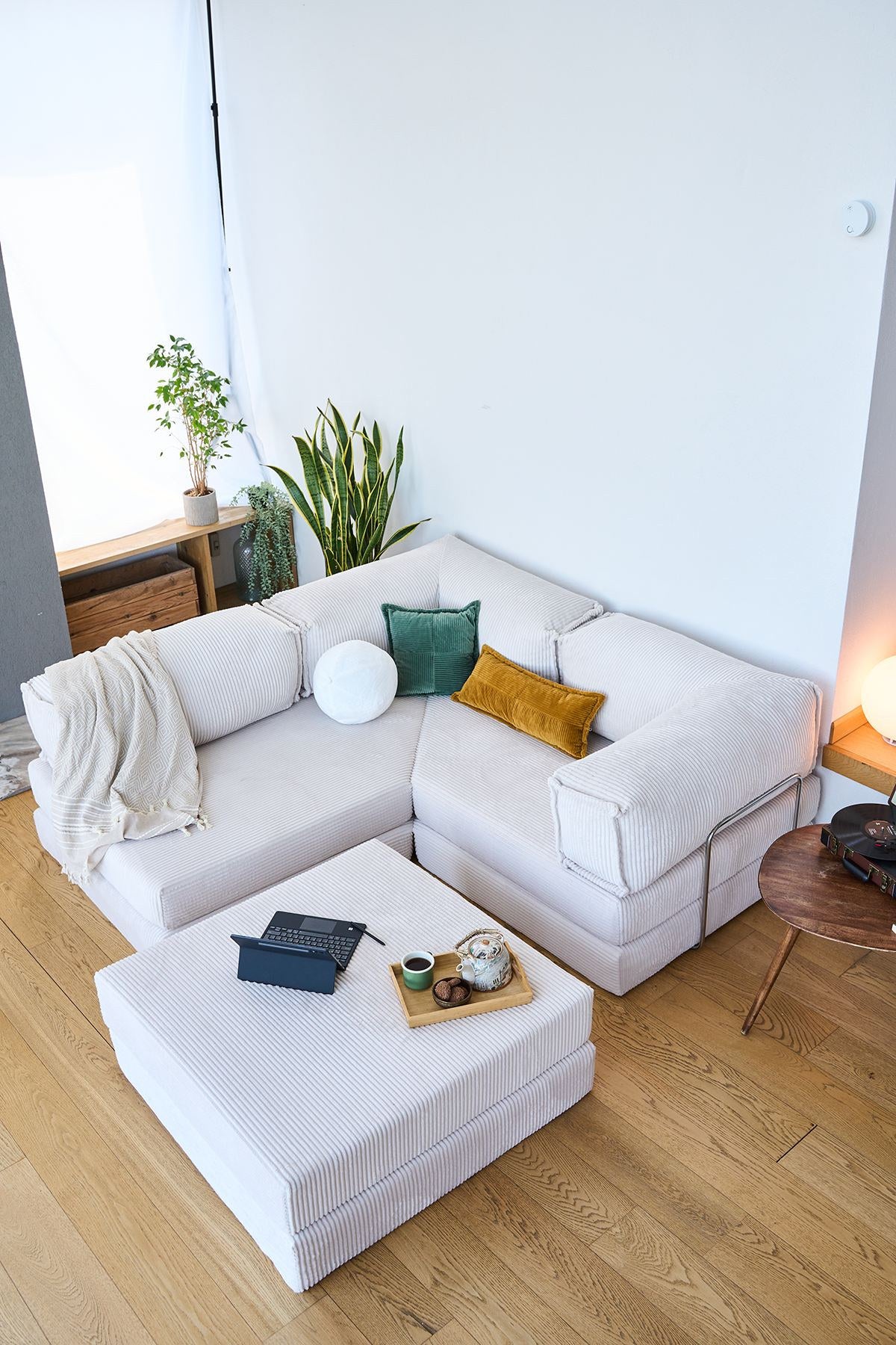Cremefarbenes Eck-Schlafsofa aus Cord-Plüschstoff mit vier Kissen, rutschfester Sohle und abnehmbarem Bezug, Frontalansicht auf hellem Untergrund.