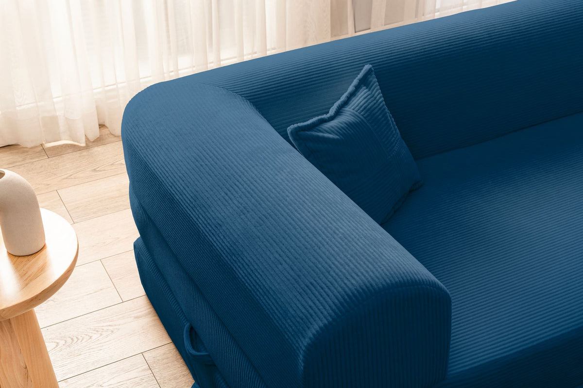 Blaues Ecksofa-Bett aus geripptem Cord-Plüschstoff mit vier Kissen, abnehmbarem Bezug und rutschfester Sohle, Frontalansicht.