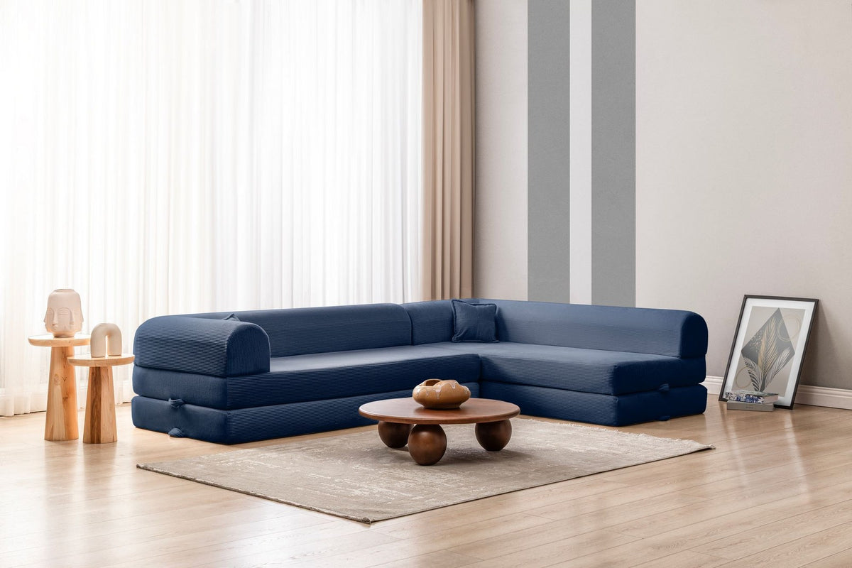 Marineblaues Ecksofa-Bett mit Cord-Plüschbezug, vier Kissen, Rückenlehne und niedriger Sitzhöhe, freistehend im Raum fotografiert.