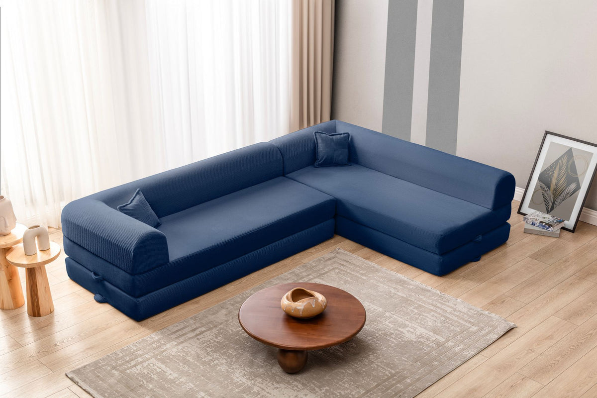 Marineblaues Ecksofa-Bett mit Cord-Plüschbezug, vier Kissen, Rückenlehne und niedriger Sitzhöhe, freistehend im Raum fotografiert.
