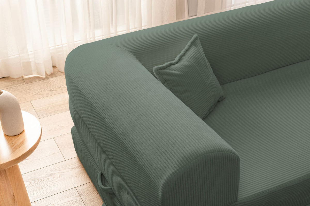 Grünes Ecksofa-Bett aus geripptem Cord-Plüschstoff mit vier Kissen, Rückenlehne und Sitzfläche aus Schaumstoff, Frontalansicht.