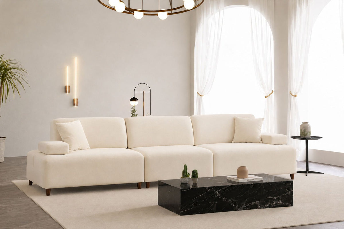 Cremefarbenes 4-Sitzer-Sofa mit hohen Kunststoffbeinen, Polyesterbezug, Buchenholzgestell und zwei losen Kissen auf hellem Hintergrund.