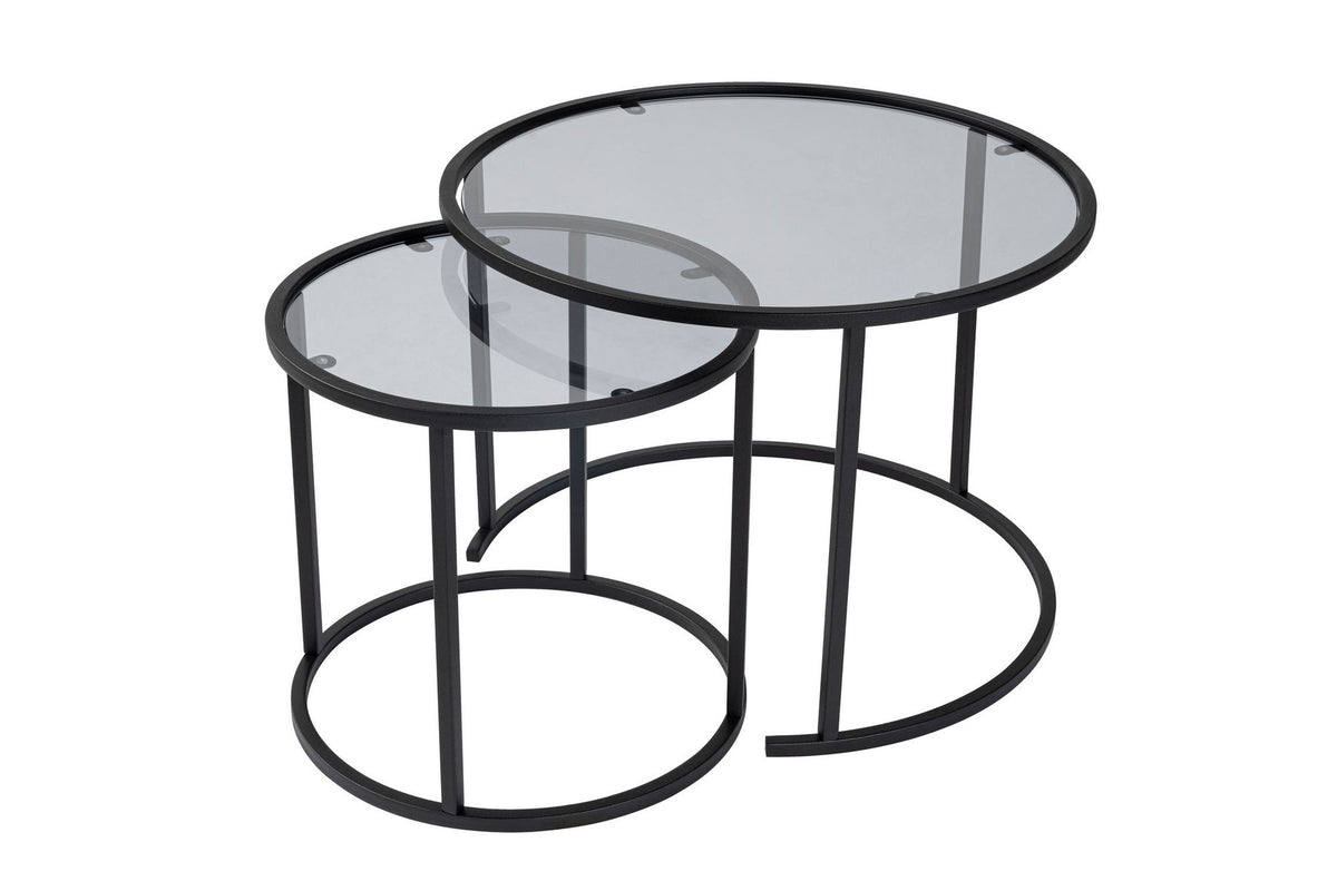 Zwei runde Couchtische unterschiedlicher Grösse mit schwarzer Glasplatte und schwarzem Metallgestell, gestapelt im Wohnzimmer.
