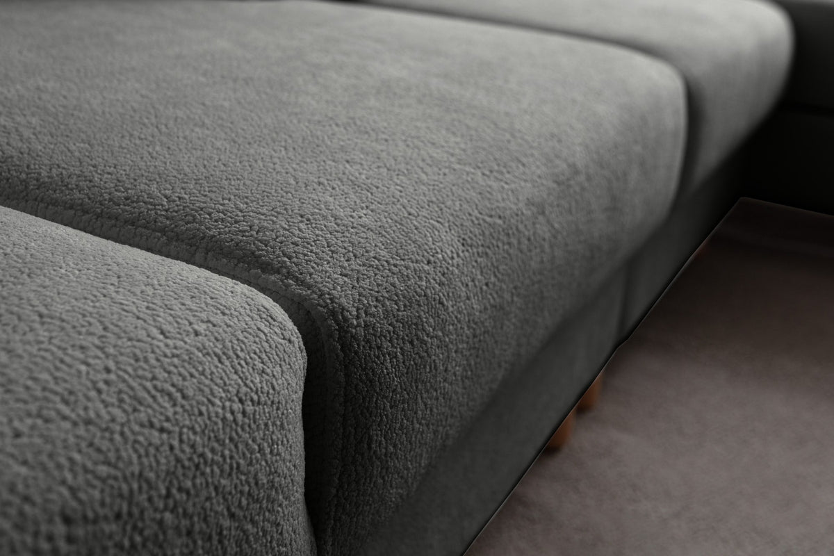 Anthrazitfarbenes Eck-Schlafsofa Aries von Hanah Home mit Coco-Boucle-Bezug, Holzbeinen und ausklappbarer Liegefläche in Wohnraumumgebung.