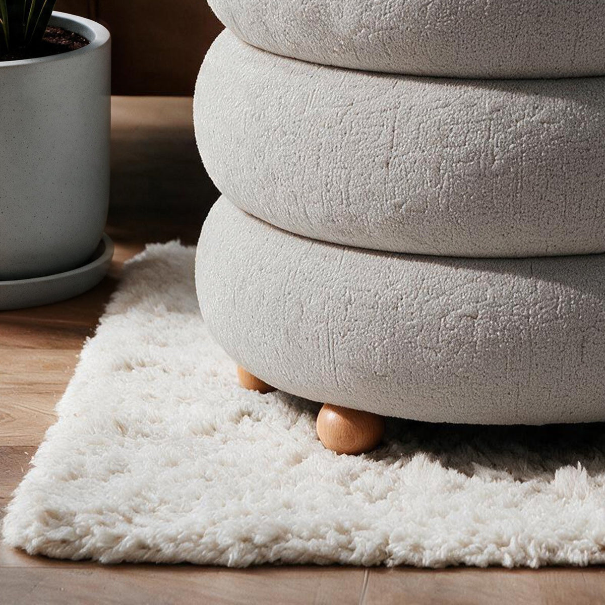 Hellgrauer Ottavia Pouf von Hanah Home mit gestricktem Polyesterbezug, gepolsterter Sitzfläche und Kugelfüssen aus Holz in kompakter Kubusform.