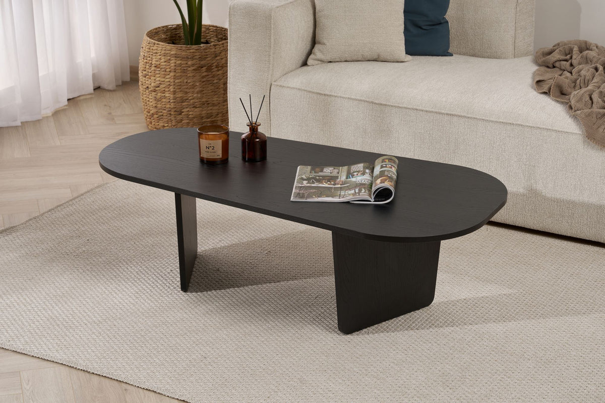 Ovaler Couchtisch aus melaminbeschichteter Spanplatte in Holz Schwarz, schlichte Form, Masse 130x65x40 cm, freistehend im Wohnraum.