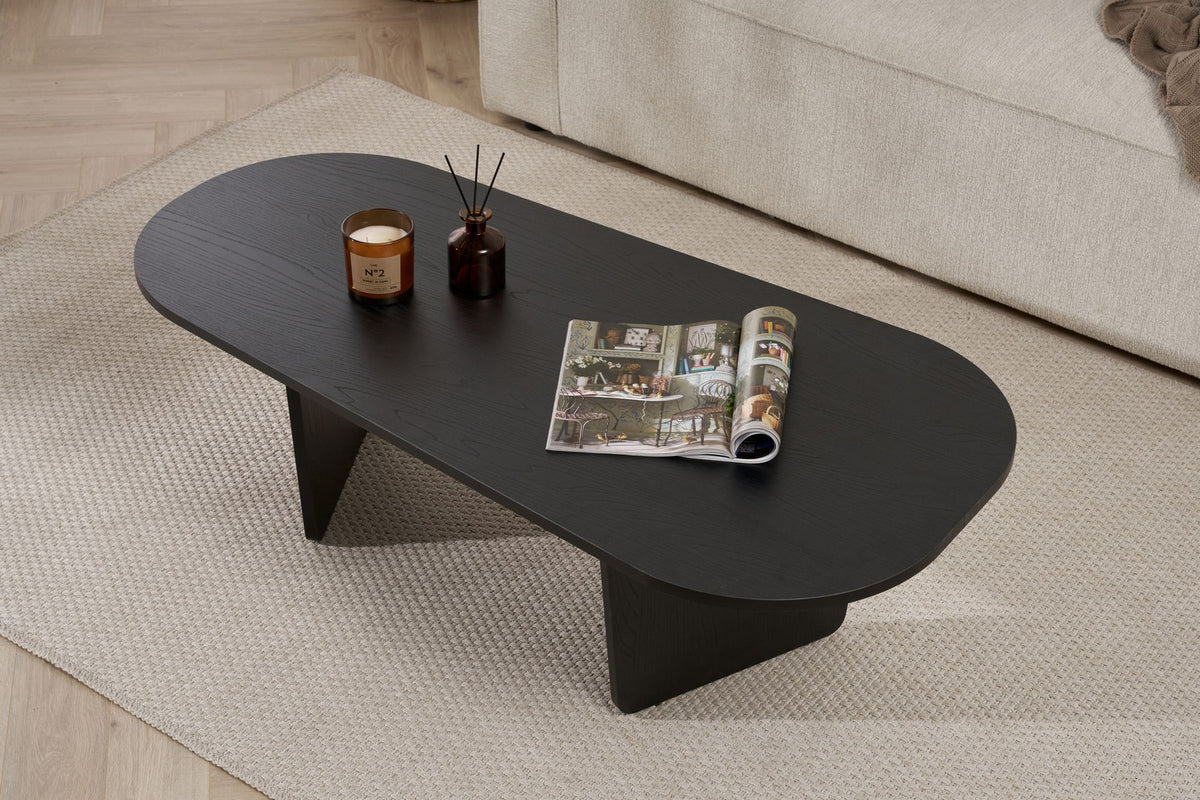Ovaler Couchtisch aus melaminbeschichteter Spanplatte in Holz Schwarz, schlichte Form, Masse 130x65x40 cm, freistehend im Wohnraum.