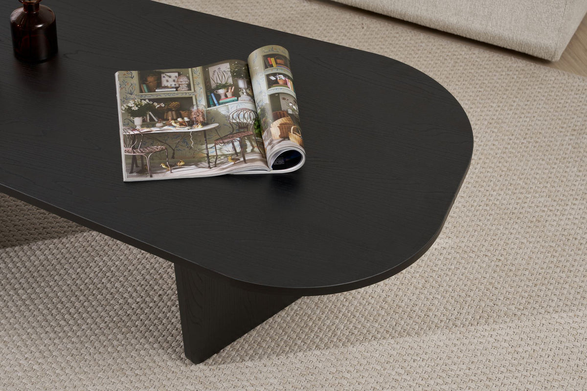 Ovaler Couchtisch aus melaminbeschichteter Spanplatte in Holz Schwarz, schlichte Form, Masse 130x65x40 cm, freistehend im Wohnraum.