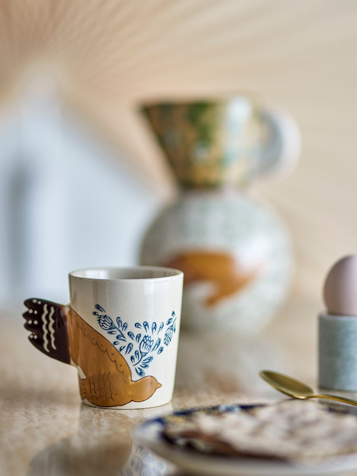 Beige Tasse aus Steinzeug der Serie Hezha von Bloomingville mit handverzierter Vogel-Illustration und Henkel in Vogelschwanz-Form