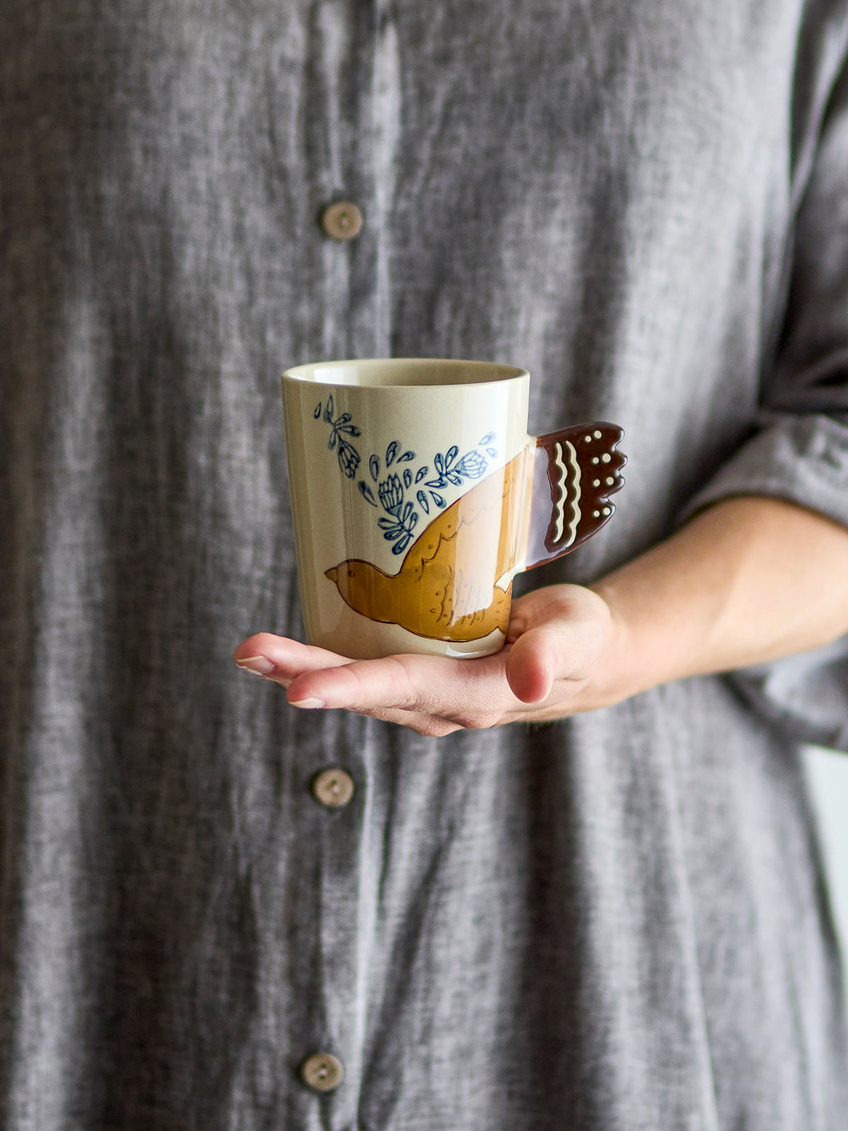 Beige Tasse aus Steinzeug der Serie Hezha von Bloomingville mit handverzierter Vogel-Illustration und Henkel in Vogelschwanz-Form