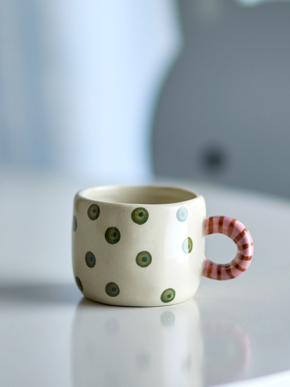 Weisse Nini Tasse aus Steingut von Bloomingville mit handbemaltem Muster, kleine runde Form mit Henkel, auf hellem Hintergrund fotografiert.