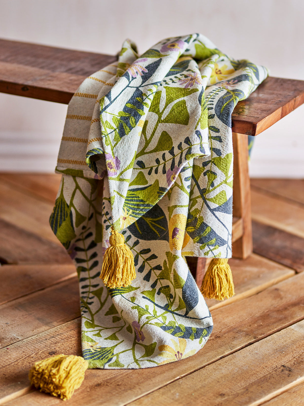 Wolldecke Camelie von Creative Collection in Bunt mit botanischem Blätter- und Blumenmuster, gewebt und bedruckt, mit gelben Quasten an den Ecken.