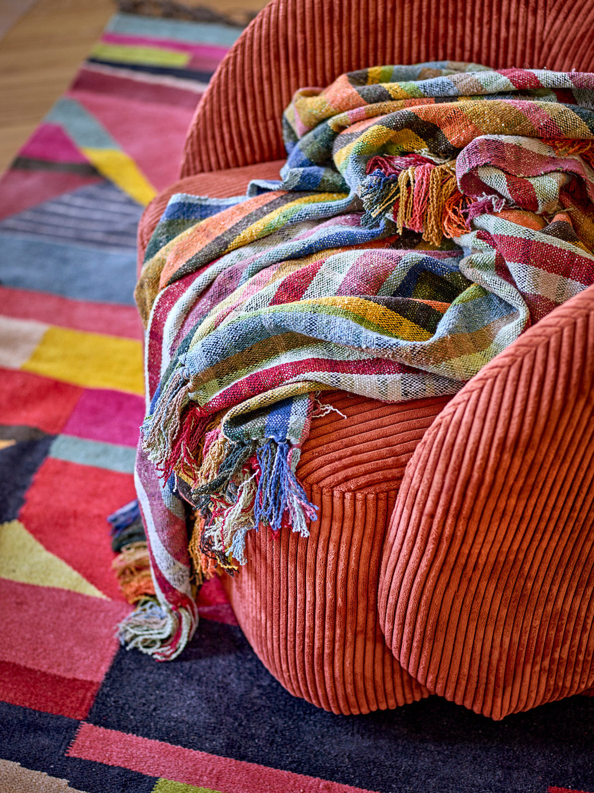 Gewebte Wolldecke Elmy von Bloomingville in Orange mit buntem Karomuster, Blau- und Rotakzenten sowie langen mehrfarbigen Fransen am Rand.