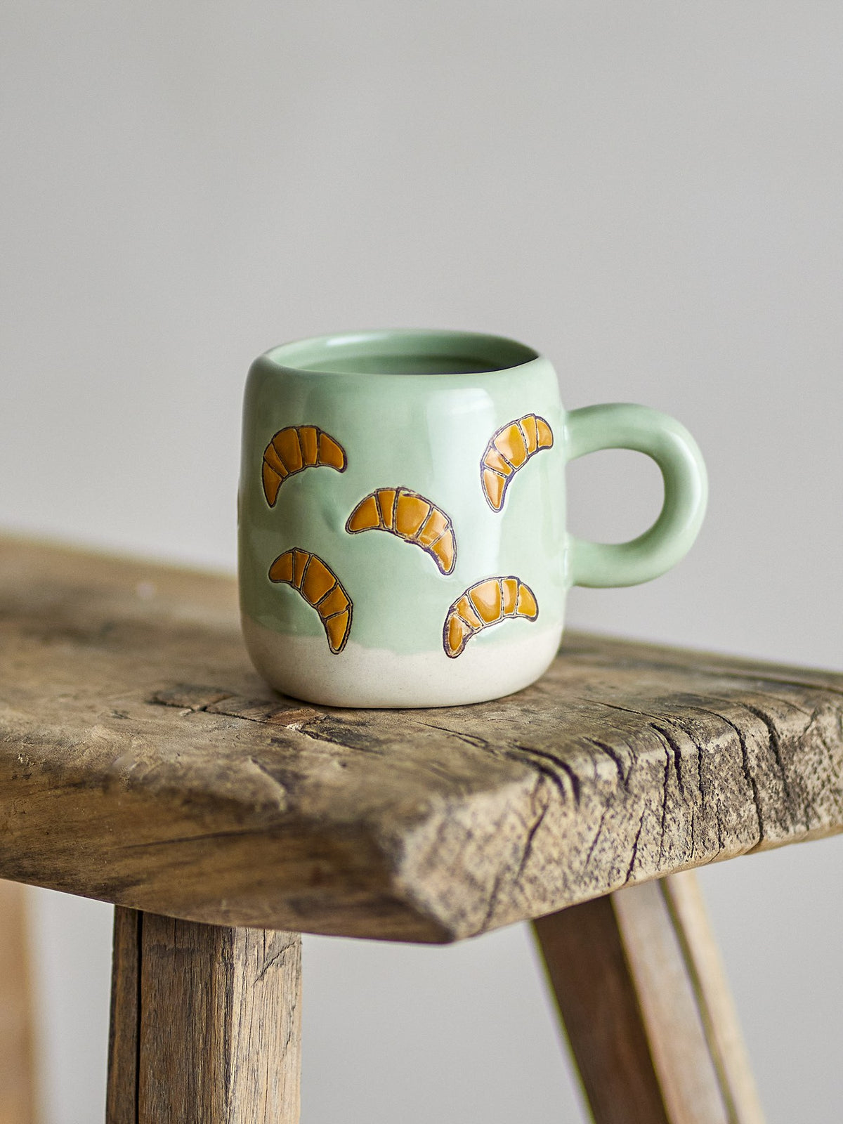Millie Tasse von Bloomingville Mini aus Steingut, handbemalt mit Croissant-Motiven in Orange, Beige und Grün, kleine runde Form.
