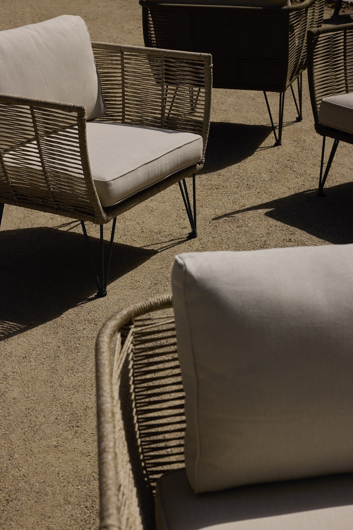 Brauner Loungesessel mit schwarzem Eisengestell, Flechtoptik und hellen Kissen, Outdoor-Sessel im Freien fotografiert.