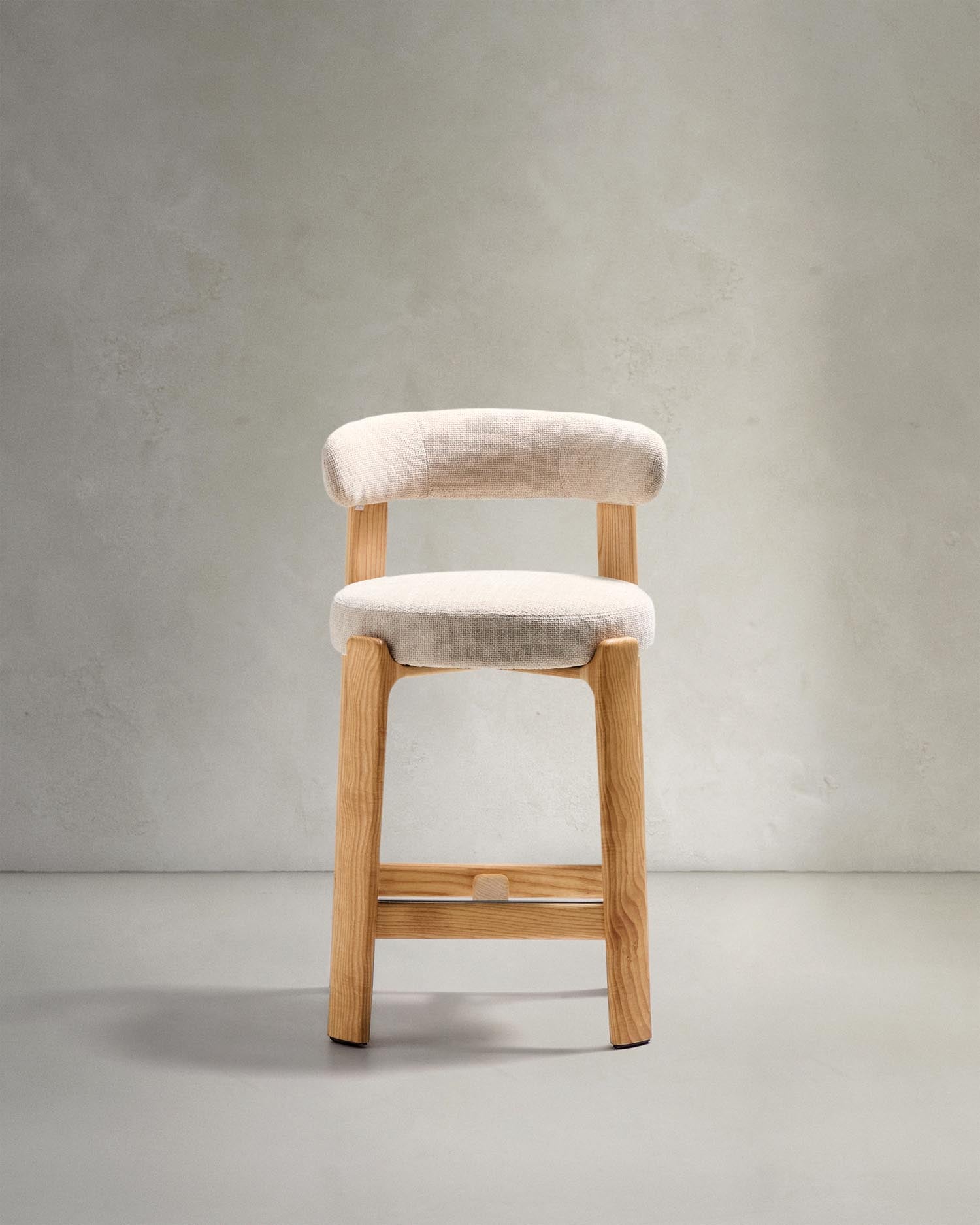 Entdecken Sie den Hocker Granite von Kave Home: Beigefarbene Chenille und massives Eschenholz vereinen sich in stilvollem skandinavischen Design.