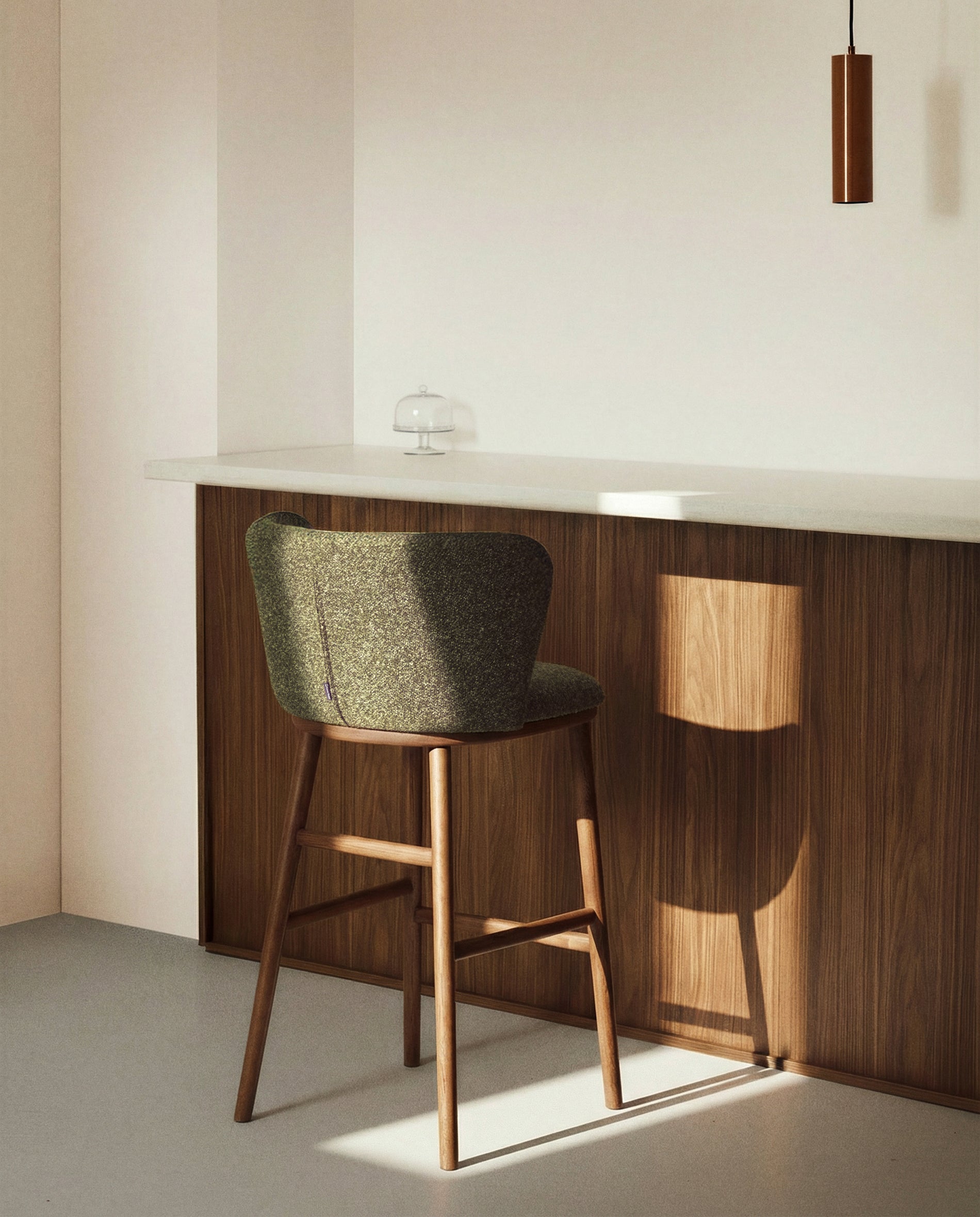 Eleganter Hocker Ciselia in tiefem Dunkelgrün, gepolstert mit Chenille, auf stabilen Eschenholzbeinen in Walnussholzoptik, ideal für stilvolle Bars.