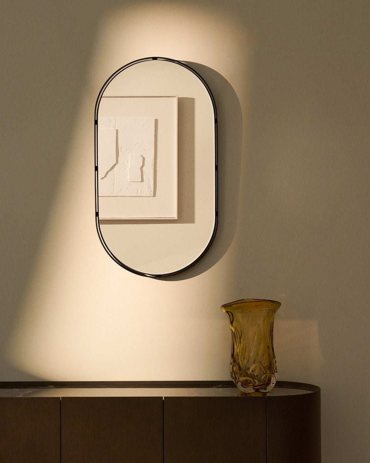 Ovaler Wandspiegel mit schwarzem Metallrahmen aus zwei konzentrischen Ringen, Glasfläche und MDF-Rückseite, an der Wand montiert.