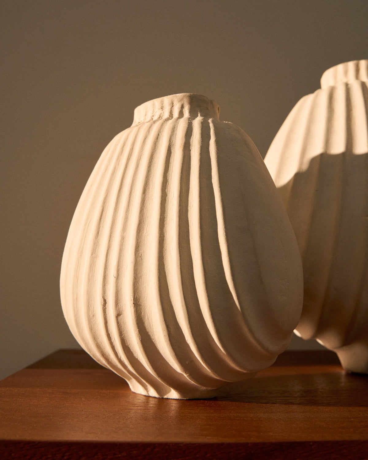 Handgefertigte Vase aus Pappmaché in der Farbe Ecru mit abgerundeter Form und feinen Relief-Linien auf der gesamten Oberfläche.