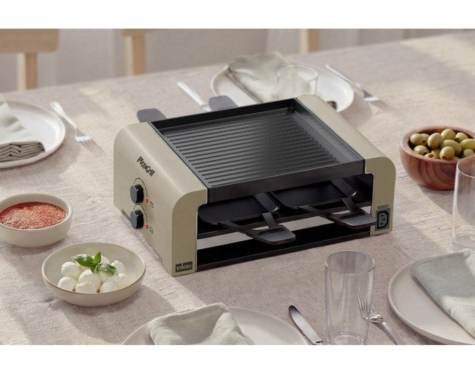 STÖCKLI Tischgrill PizzaGrill 4 Connect in Ivory Gold mit wendbarer Aluguss-Grillplatte, vier Pfännchen und Kunststoffspachteln auf dem Esstisch.