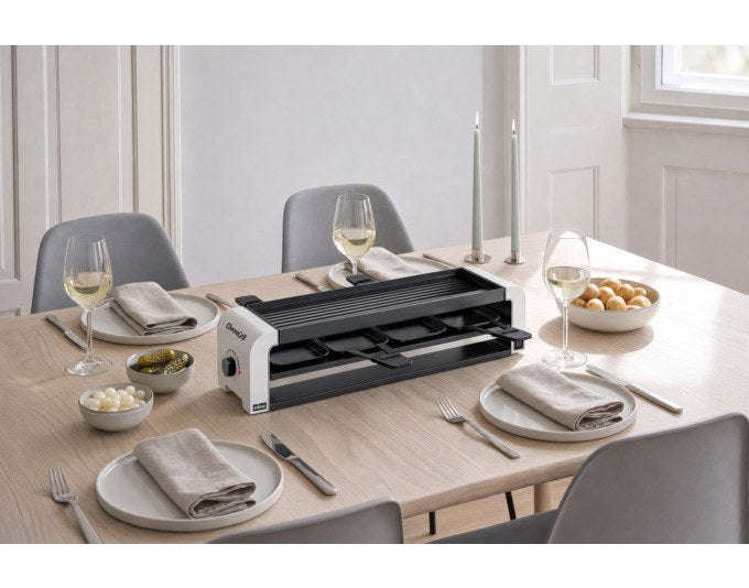 Weisser STÖCKLI Tischgrill CheeseGrill 4 Connect mit wendbarer Grillplatte, vier Pfännchen und Kunststoffspachteln auf hellem Untergrund.