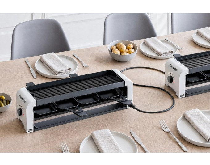 Weisser STÖCKLI Tischgrill CheeseGrill 4 Connect mit wendbarer Grillplatte, vier Pfännchen und Kunststoffspachteln auf hellem Untergrund.