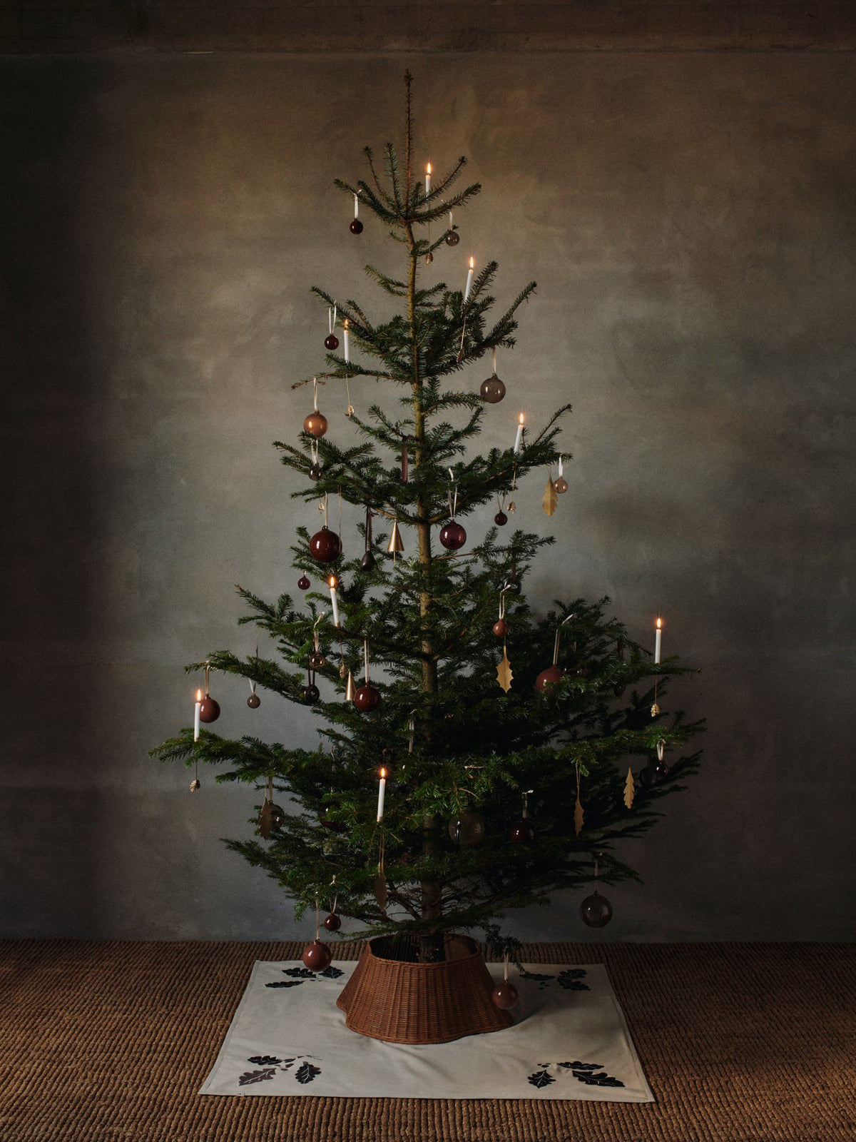 Runde Weihnachtsbaumdecke aus natürlicher Bio-Baumwolle mit aufgestickten Eichenblättern, Beeren und Sternen in dunklem Schokoladenton am Rand.