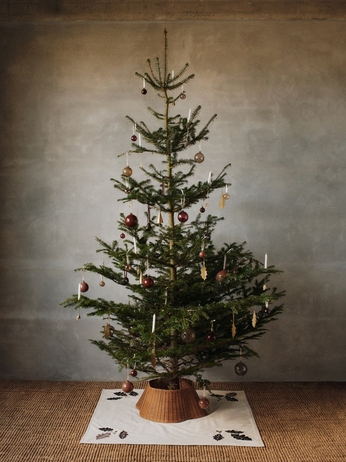 Runde Weihnachtsbaumdecke aus natürlicher Bio-Baumwolle mit aufgestickten Eichenblättern, Beeren und Sternen in dunklem Schokoladenton am Rand.