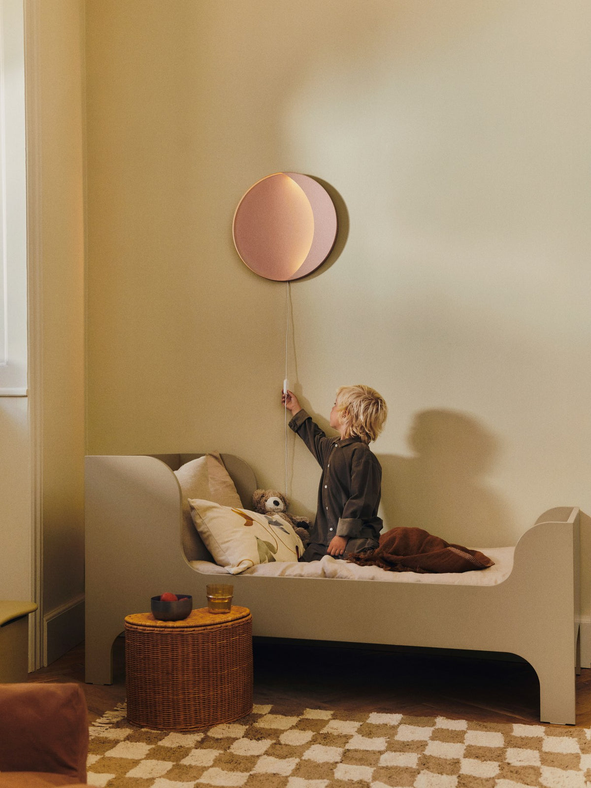 Wandleuchte Neba von Ferm Living in Tea Green, mondsichelförmig aus pulverbeschichtetem Eisen, leicht abgesetzte Metallform an heller Wand.