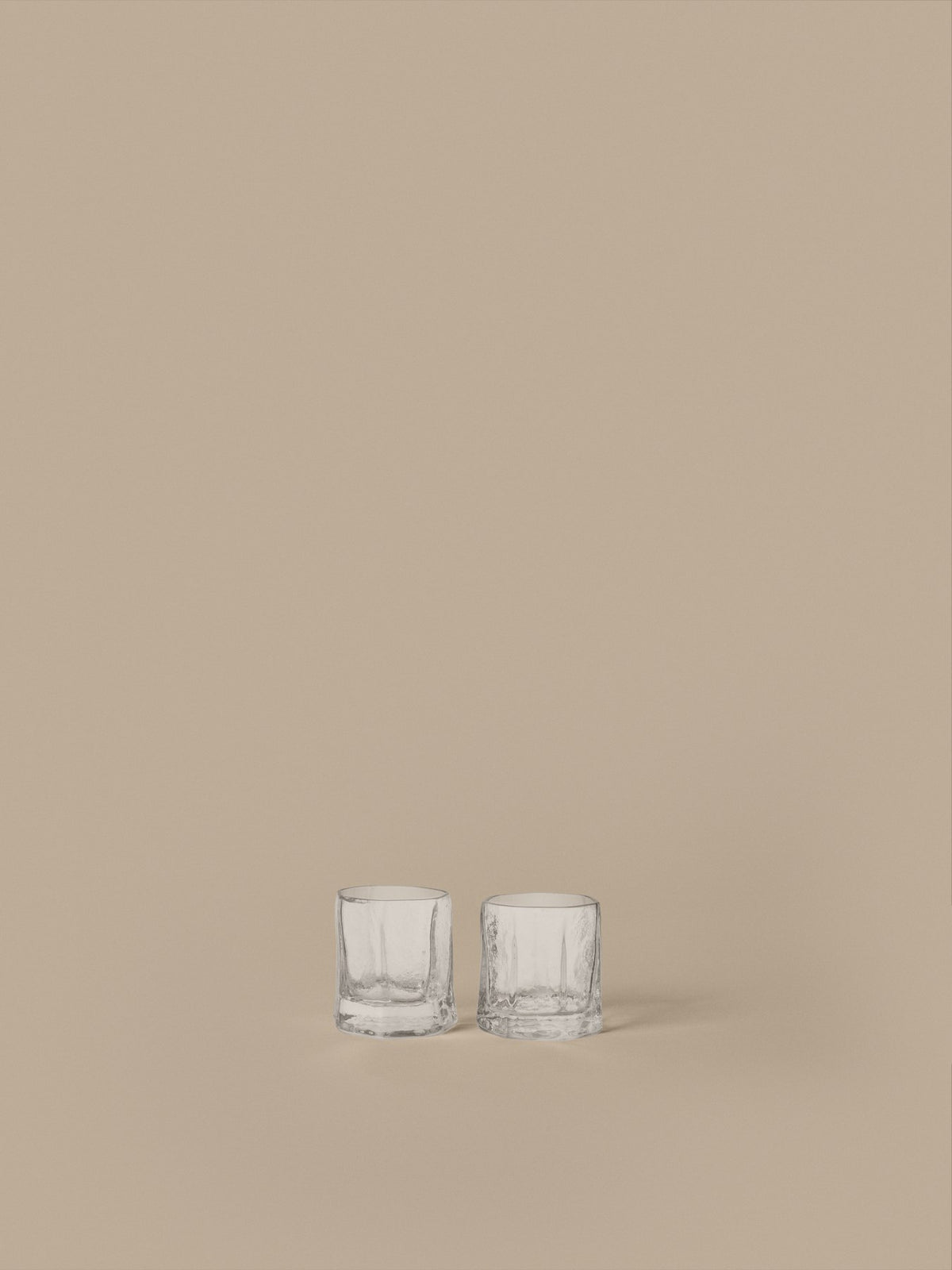 Zwei klare Kiru Gläser von Ferm Living aus mundgeblasenem recyceltem Glas mit skulpturaler, keramikähnlicher Oberflächenstruktur auf hellem Hintergrund.