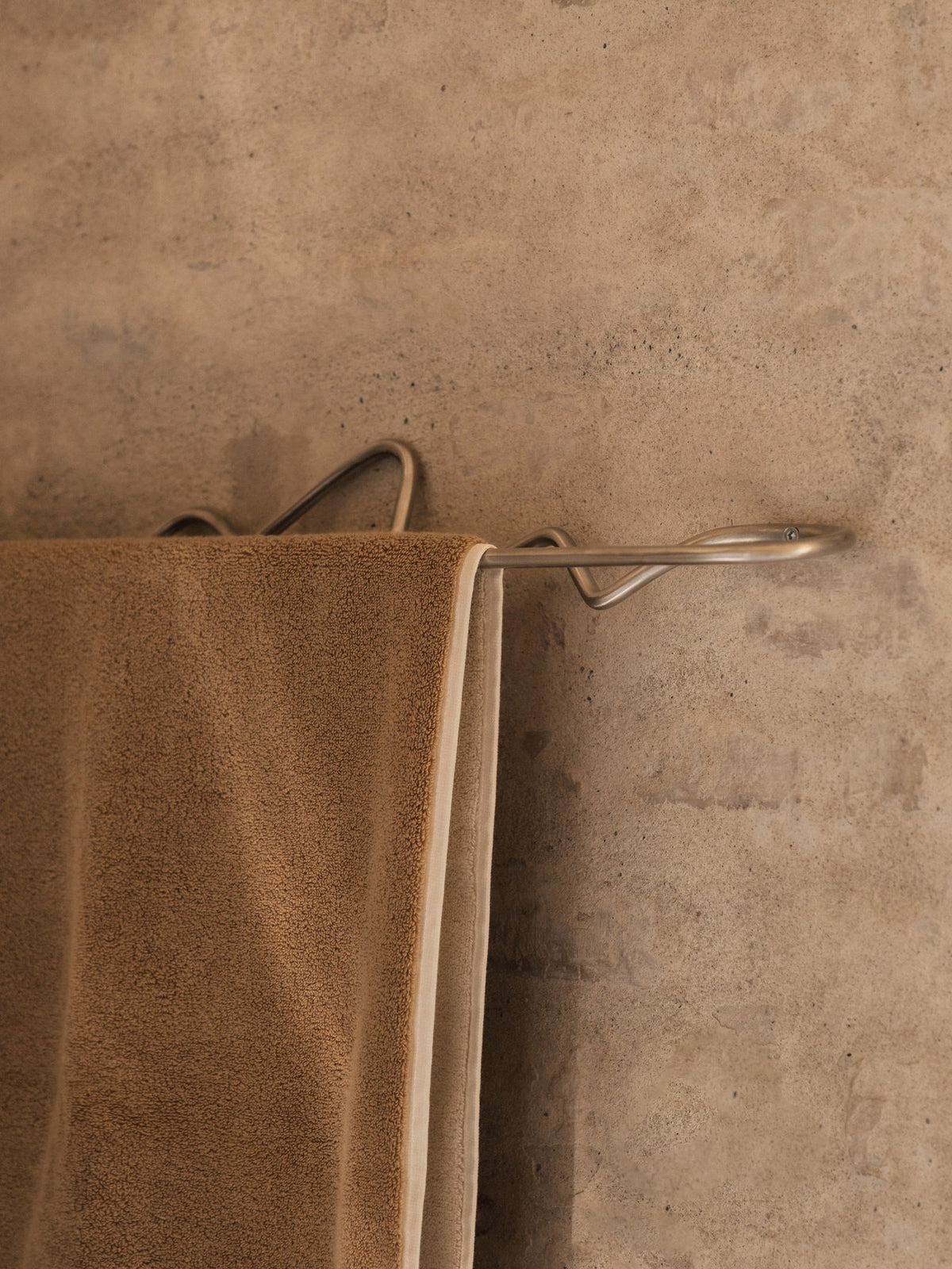Curvature Handtuchhalter von Ferm Living aus Edelstahl mit geschwungener, skulpturaler Form, montiert an einer Badezimmerwand.
