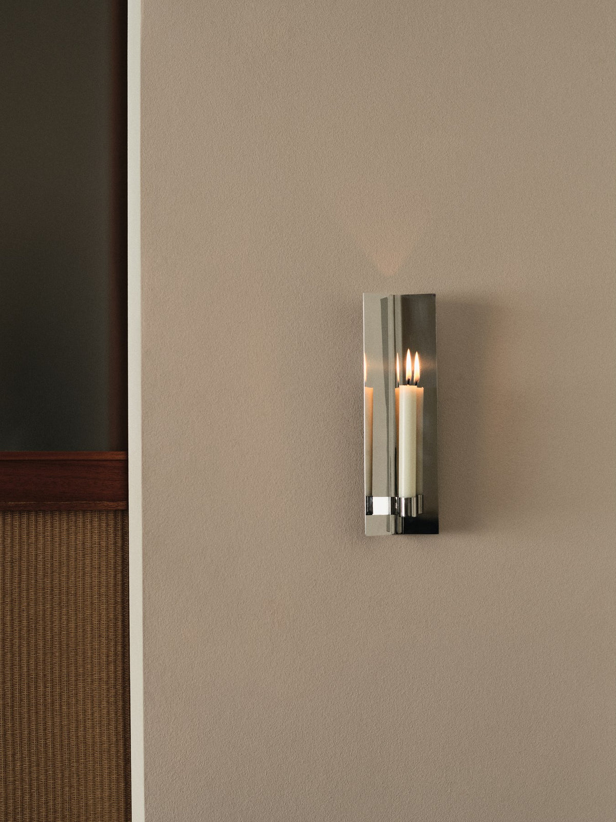 Eddy Wandkerzenhalter von Ferm Living aus spiegelpoliertem Edelstahl, schlichte gefaltete Form, montiert an weisser Wand.