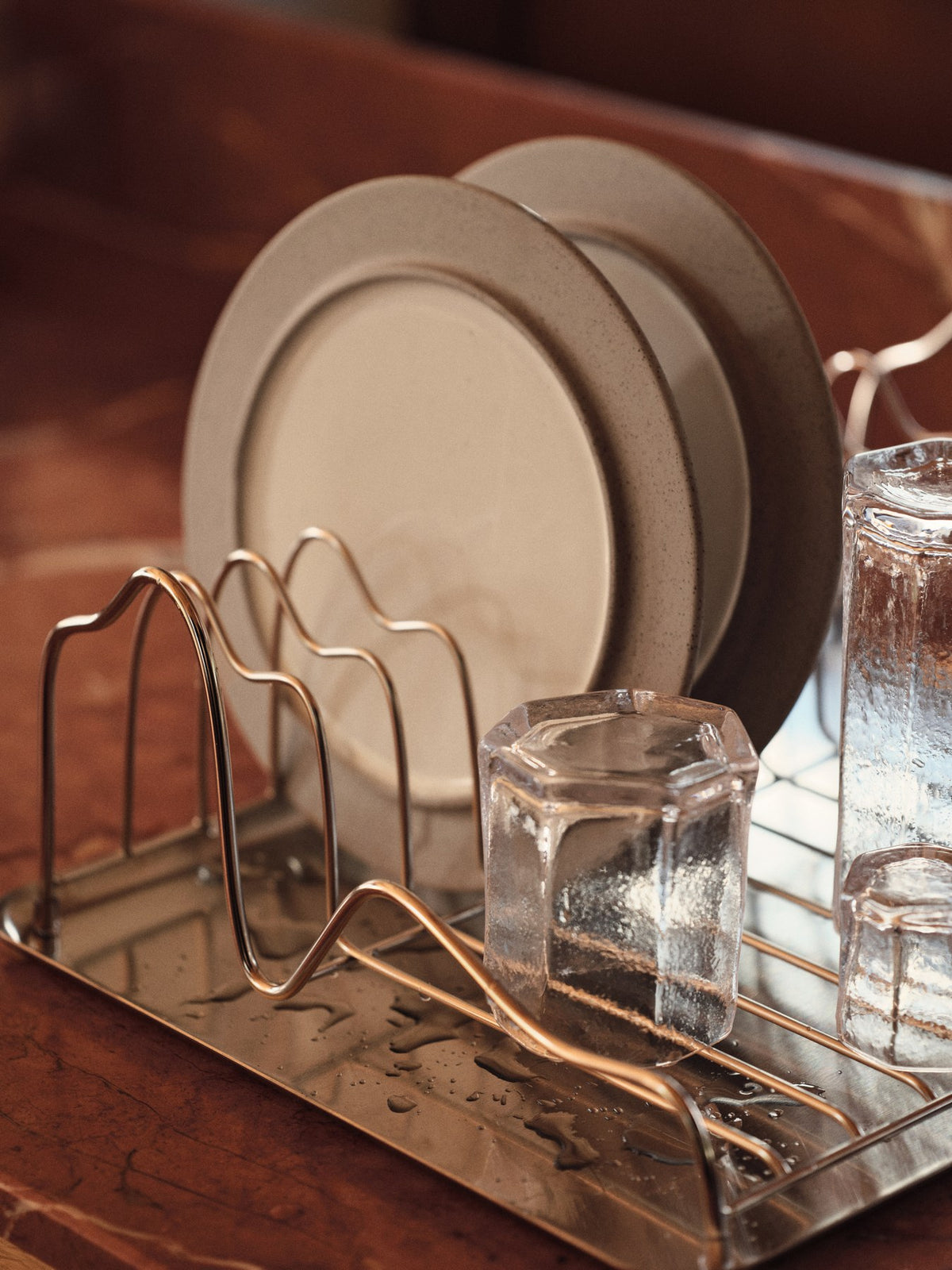 Abtropfgestell Curvature von Ferm Living aus spiegelpoliertem Edelstahl, geschwungene Form, mit passender Abtropfschale auf Küchenarbeitsplatte.