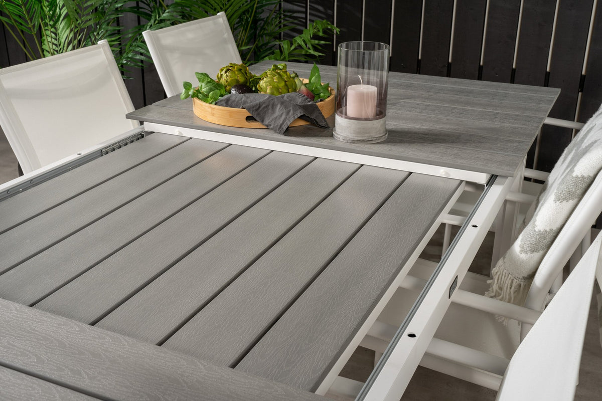 Ausziehbarer Gartentisch mit grauer Aintwood-Tischplatte und Aluminiumbeinen, umgeben von sechs weissen, stapelbaren Santorini Stühlen aus Aintwood und Aluminium.