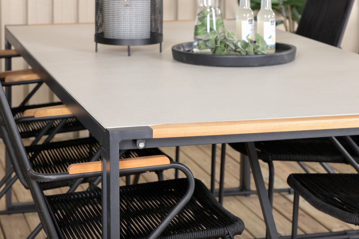 Zwei schwarze Esszimmerstühle aus Aluminium und Teakholz neben einem rechteckigen Esstisch mit Glas-Teak-Platte in Hellgrau.