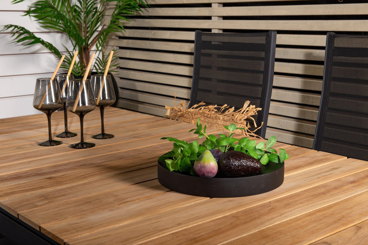 Zwei schwarze Relaxsessel Copacabana aus Aluminium mit Pulverbeschichtung neben rechteckigem Teak-Esstisch Mexico in Natur, Gartenmöbel-Set.