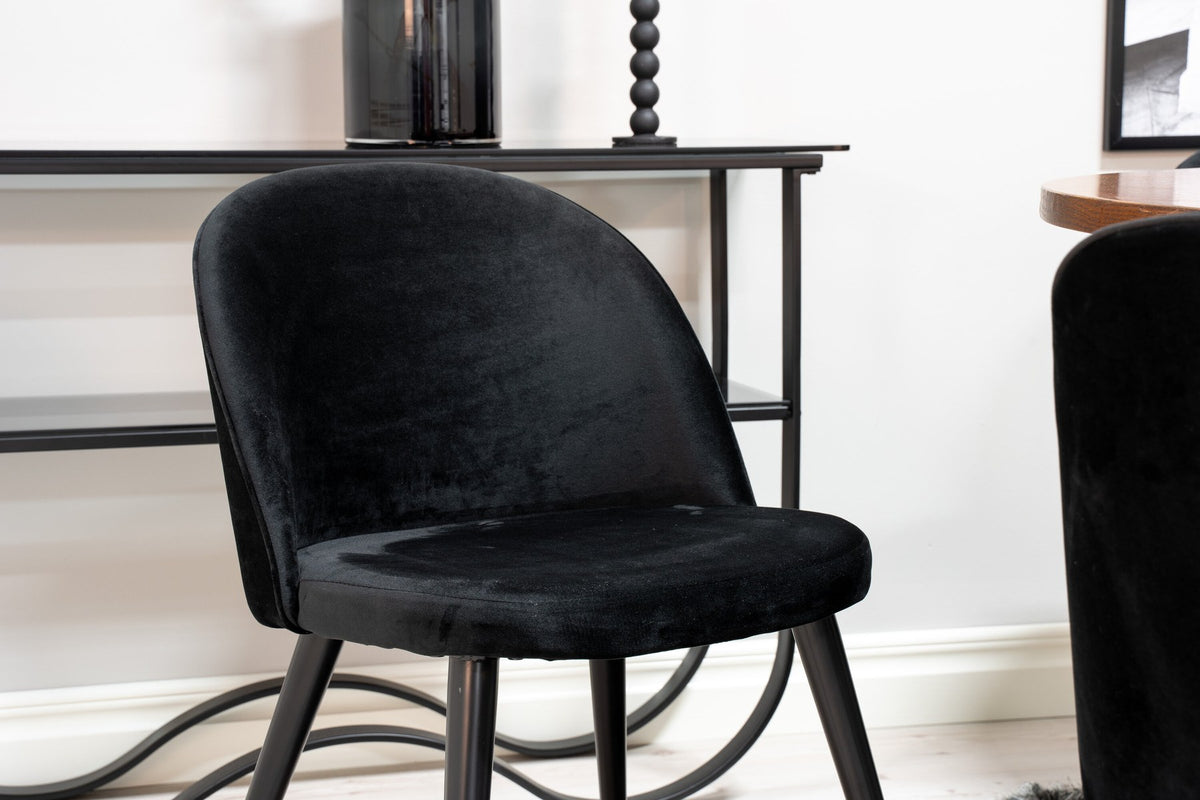 Runder Esstisch ⌀140 cm mit brauner Tischplatte aus MDF und Furnier, Stahlbeine, dazu zwei schwarze Velvet-Stühle mit pulverbeschichtetem Gestell.