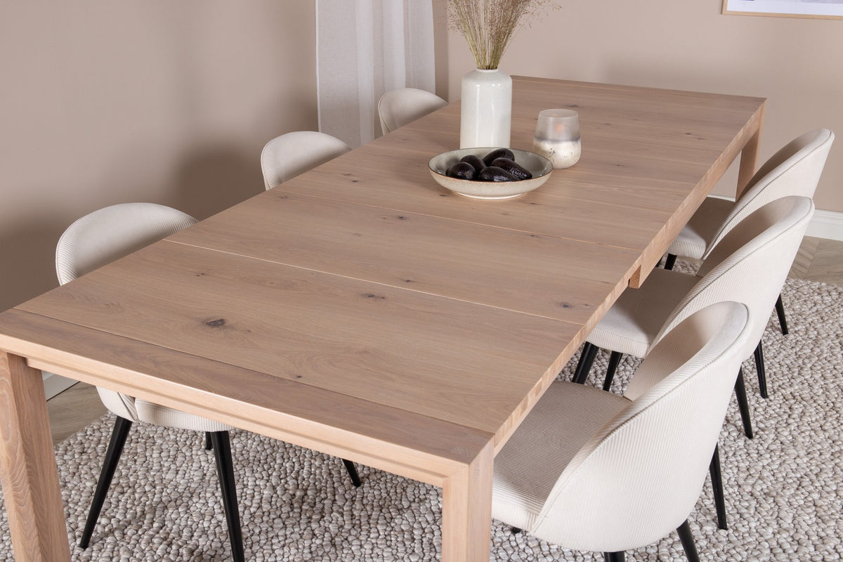 Esstisch mit heller Holzplatte in Naturfarbton auf Eichen-Gestell, umgeben von cremefarbenen Polsterstühlen aus Samt der Velvet-Serie.
