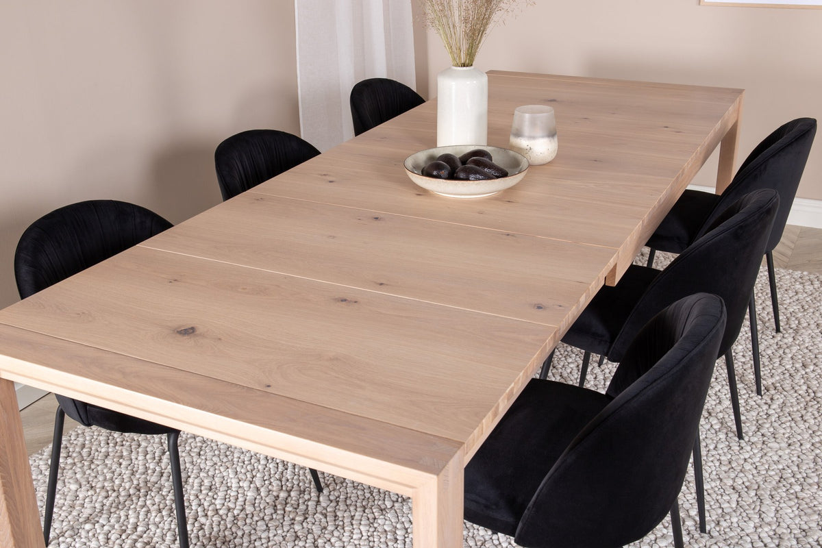 Rechteckiger Esstisch aus Eiche mit weissgelaugter Tischplatte, kombiniert mit zwei schwarzen Esszimmerstühlen im skandinavischen Design.