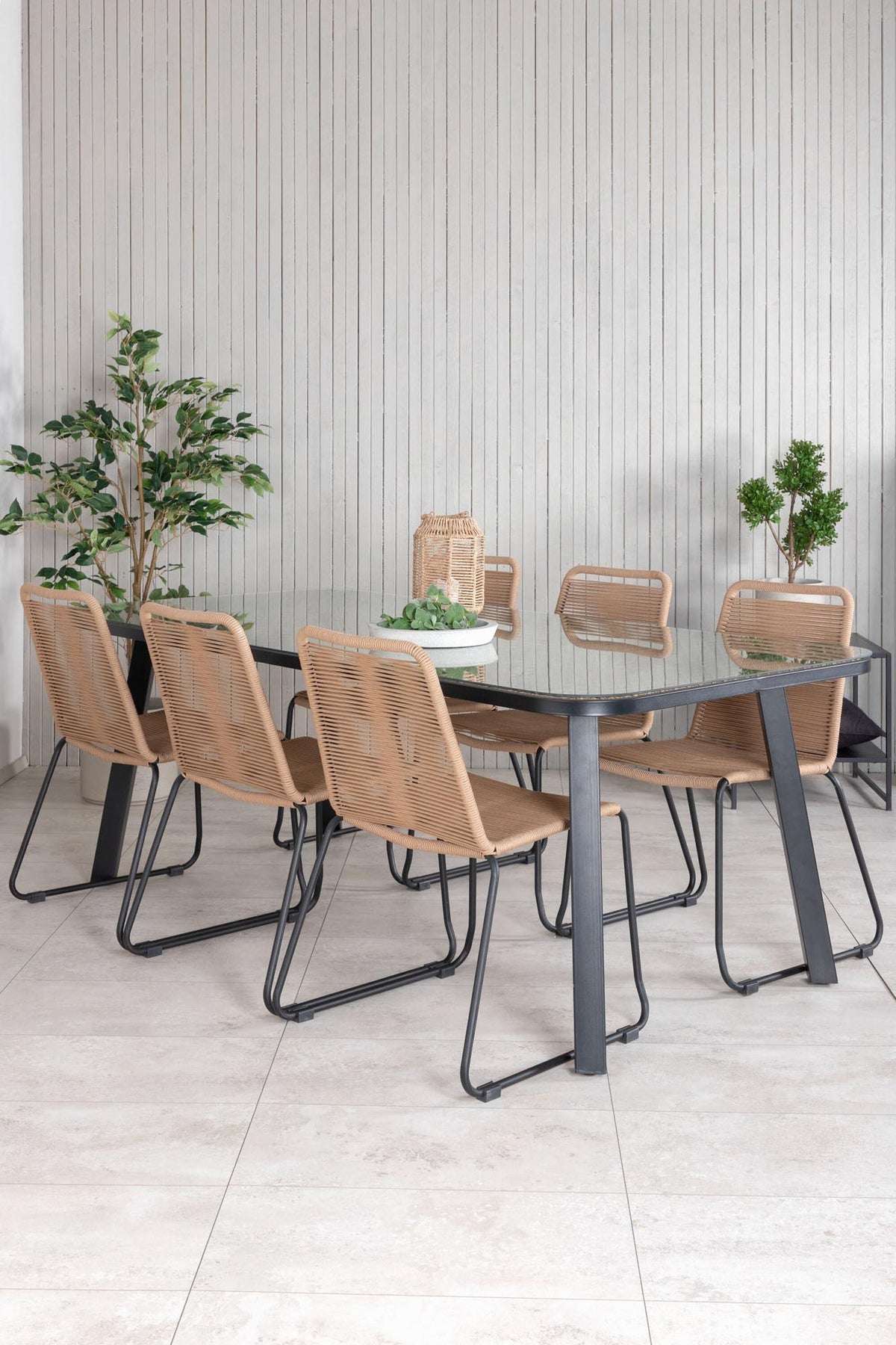 Gartentischset Paola mit schwarzem Stahlgestell und Weidengeflecht-Tischplatte sowie sechs stapelbaren Lindos-Stühlen aus schwarzem Aluminium und Polyesterseil.