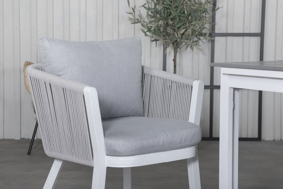 Zwei graue Esszimmerstühle mit Seil-Bezug und Aluminiumgestell neben einem weissen, ausziehbaren Aintwood-Esstisch im Garten.